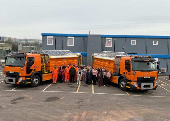 Two lorries parked diagonally with people celebrating in the middle.